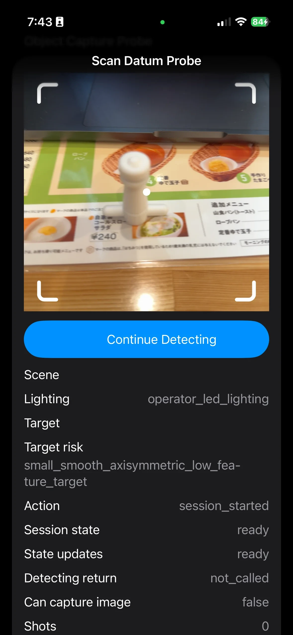 The ObjectCapture debug screen on the device. The camera view shows the part (a stopcock plug), and the HUD at the bottom reads Action: session_started, Detecting return: not_called, Can capture image: false, Shots: 0 (internal identifiers masked)