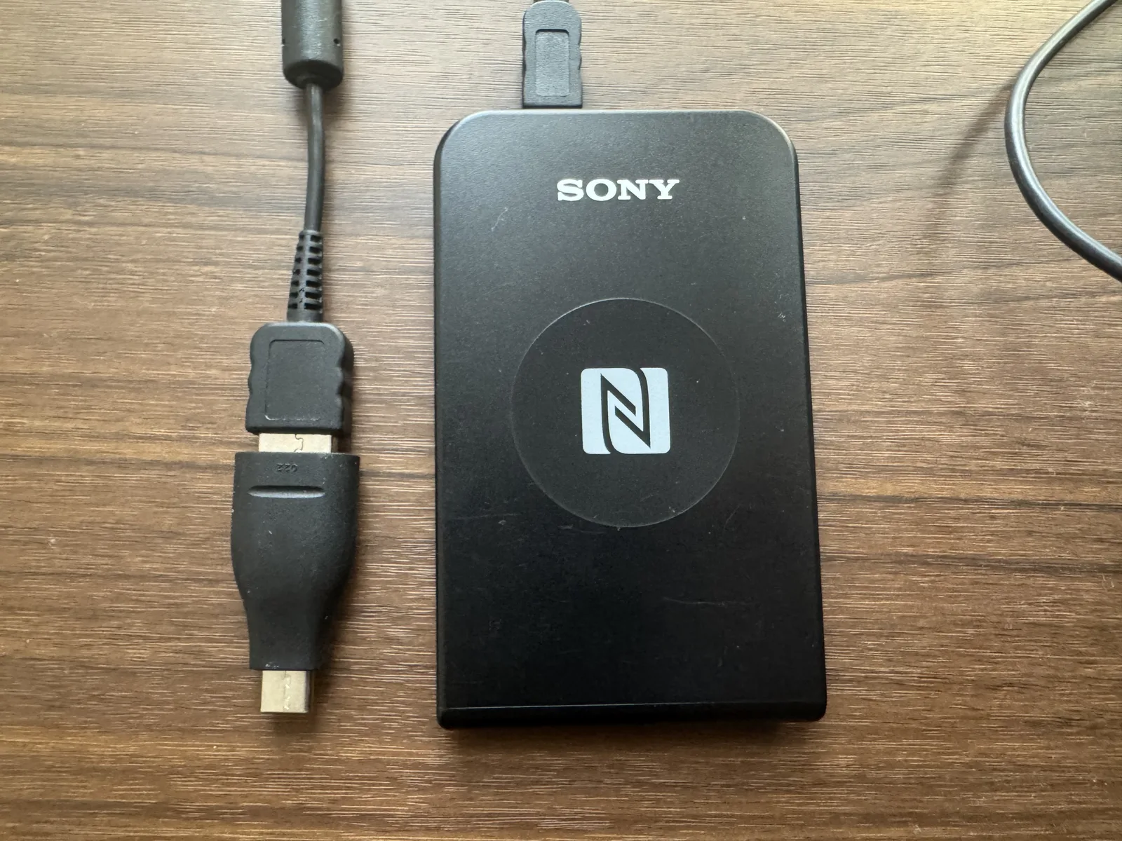 收到的 SONY PaSoRi RC-S380 机身（黑色、带 NFC 标识）与随附的 USB 数据线。没有包装盒和说明书，只有机身和数据线
